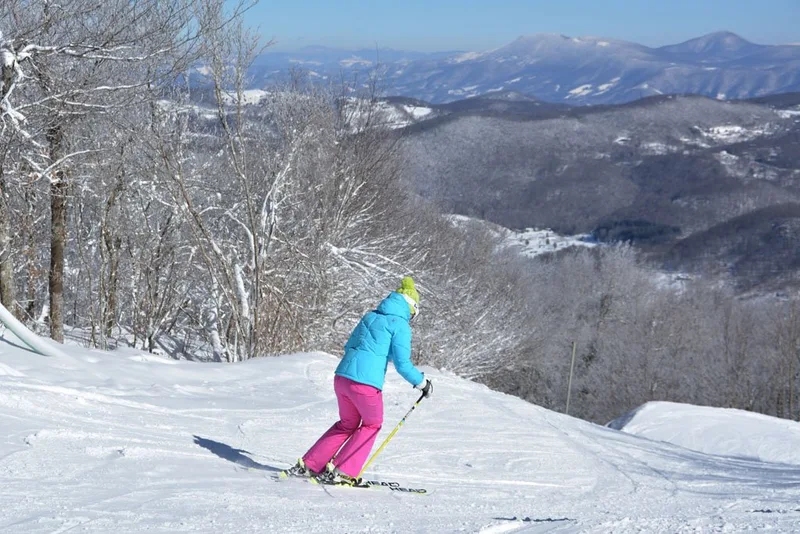 A skier descending a snowy Sugar Mountain slope with Blue Ridge peaks beyond